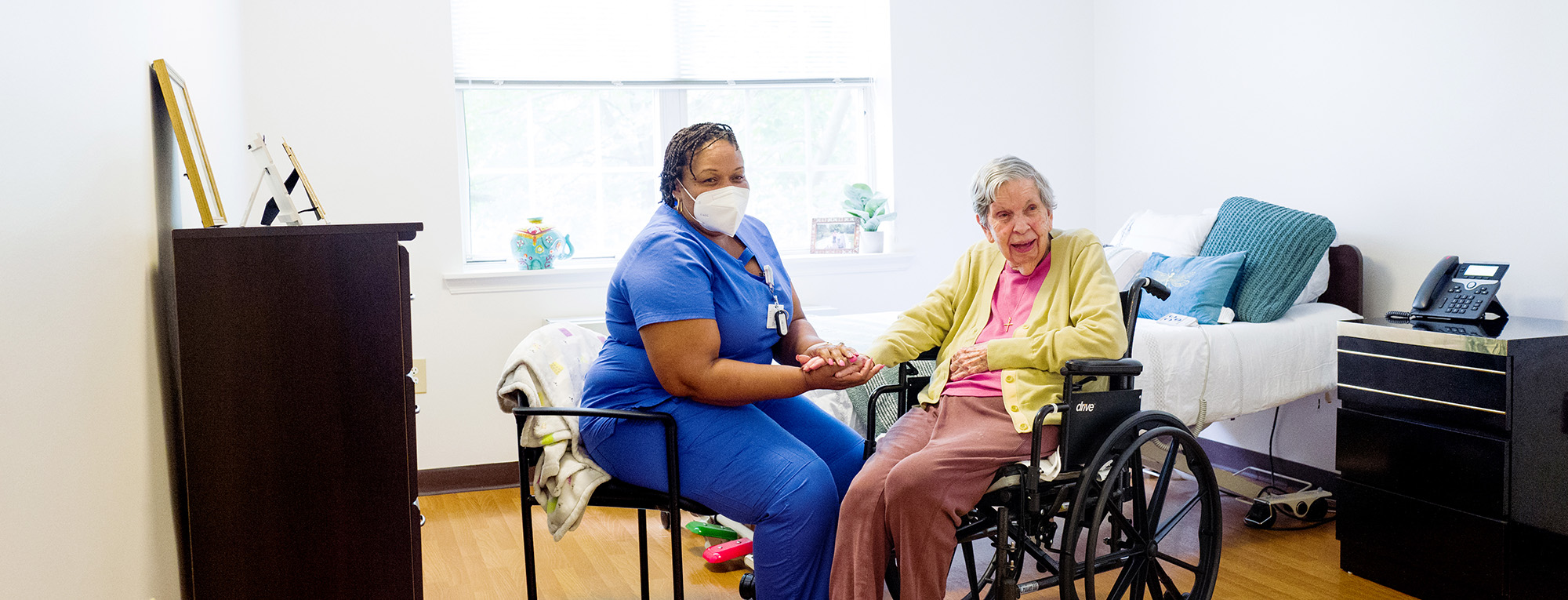 senior woman in wheelchair holding hand of caregiver