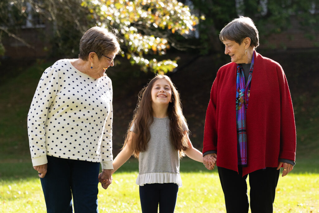 two women holding hands with young girl walking outside in brightly lit field