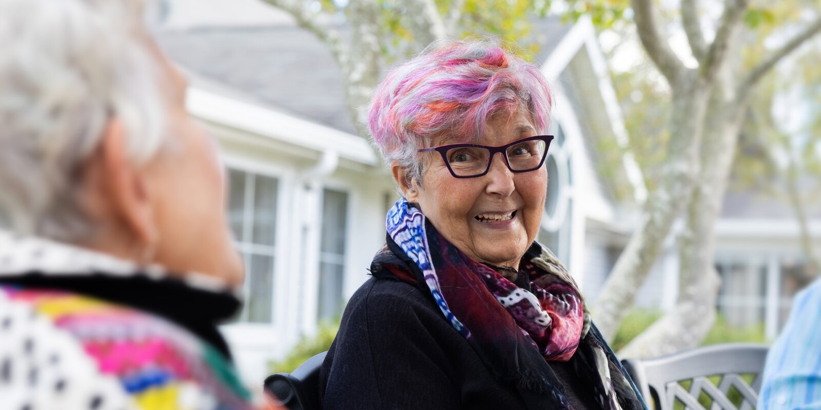 resident with pink, purple hair smiling and chatting with other resident. 